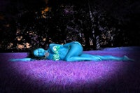 a woman laying in the grass with blue paint on her body